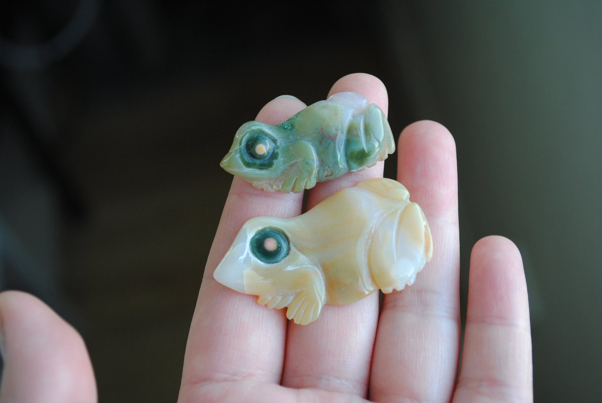 Two small stone frog carvings held in a hand against a blurred background