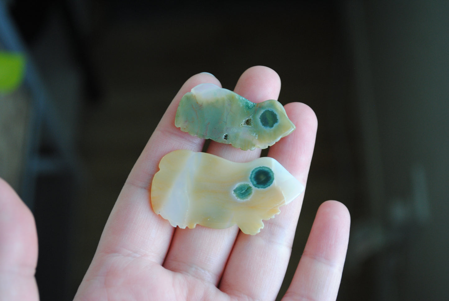 Two small stone frog carvings held in a hand against a blurred background