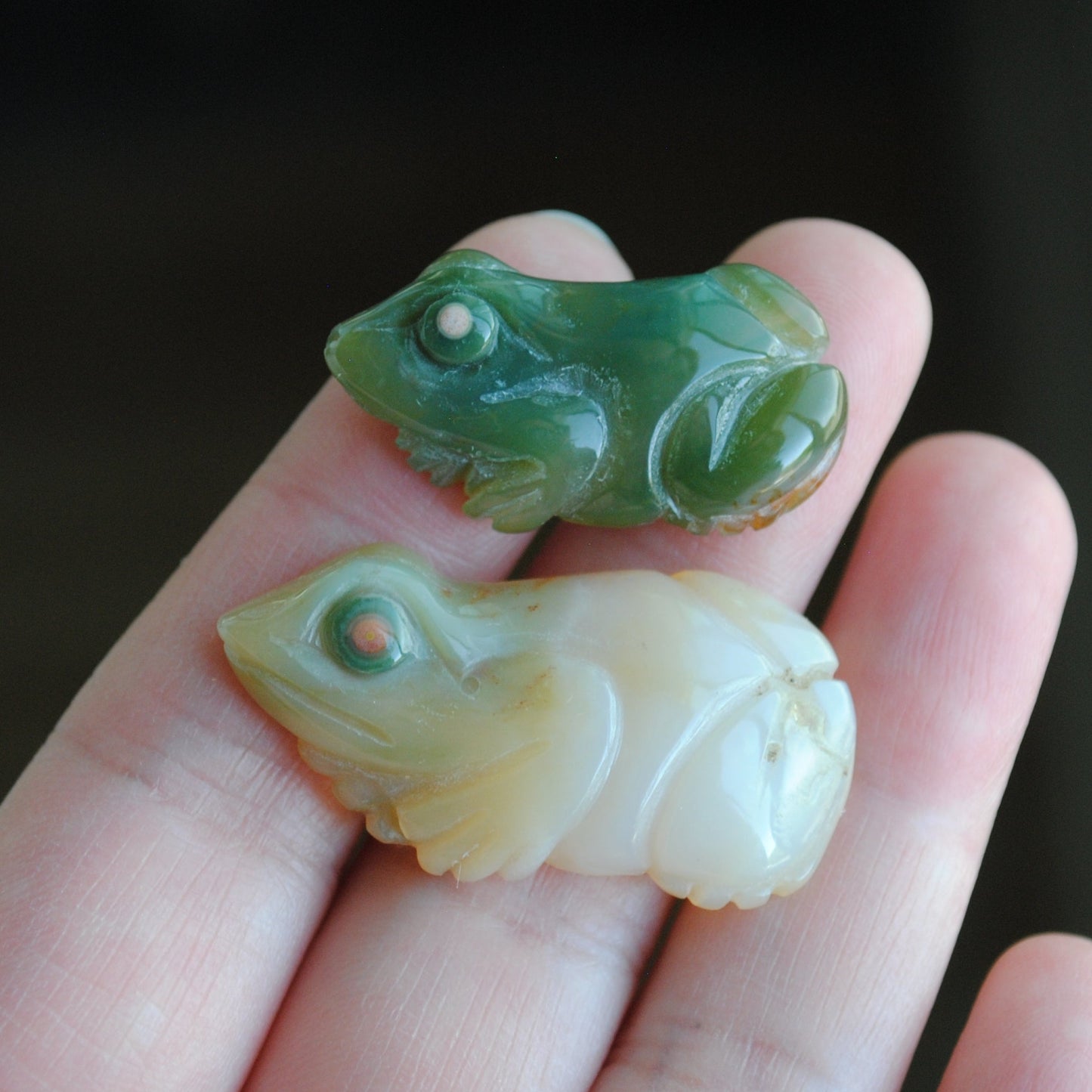 Two small stone frog carvings held in a hand against a blurred background