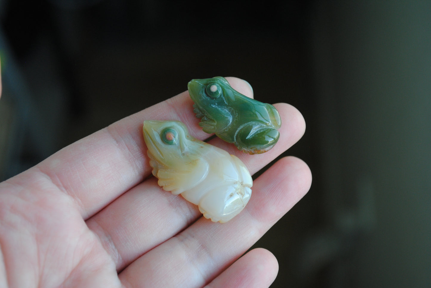 Two small stone frog carvings held in a hand against a blurred background