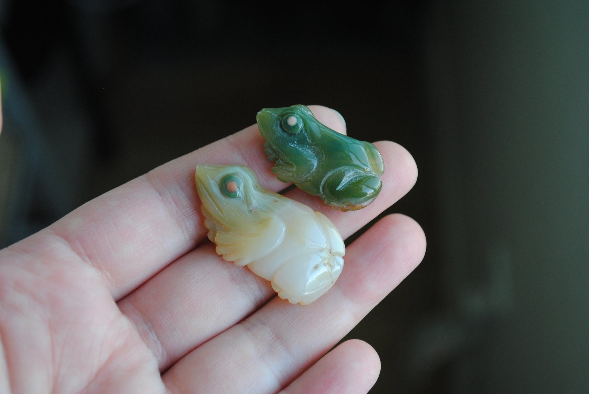 Two small stone frog carvings held in a hand against a blurred background