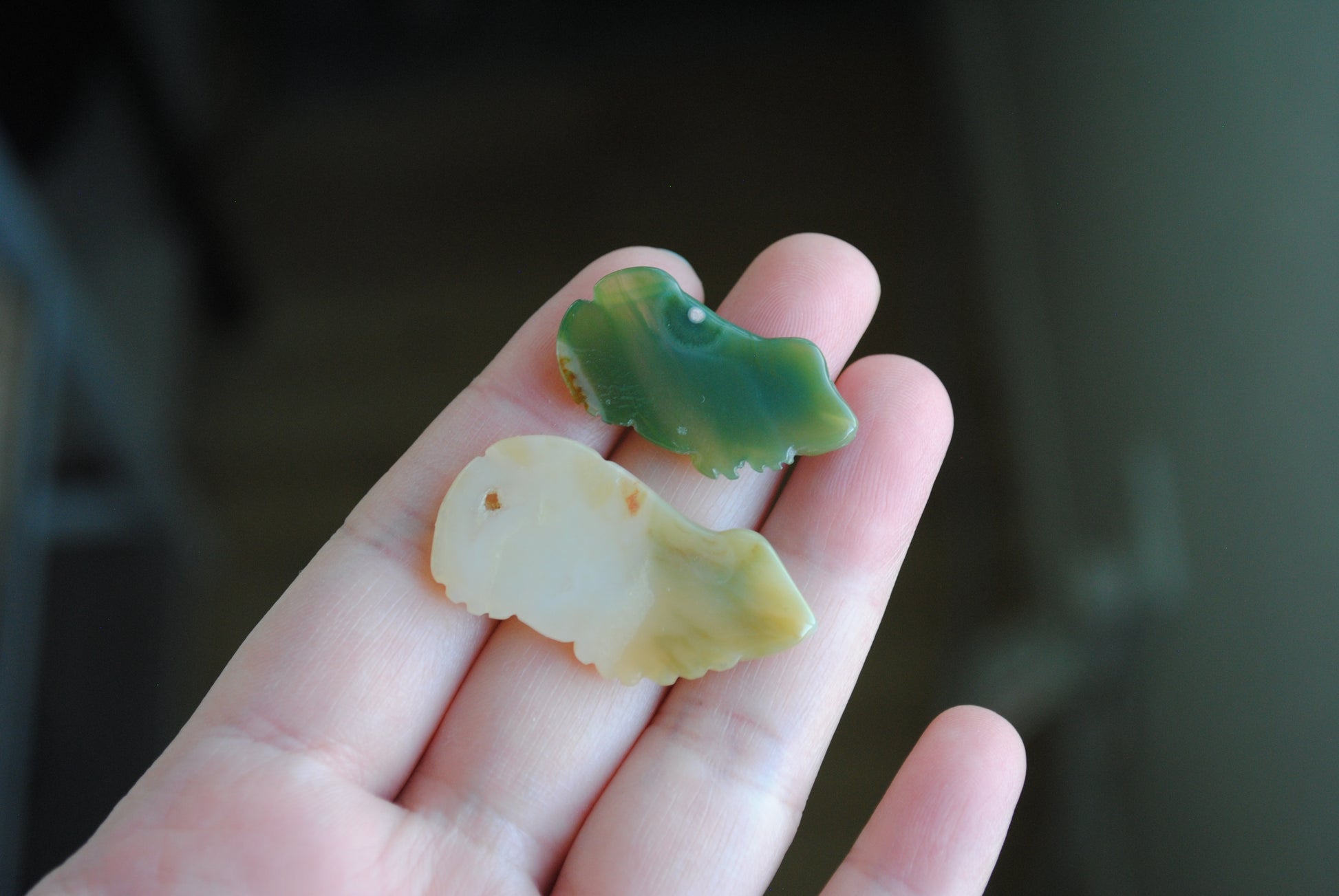 Two small stone frog carvings held in a hand against a blurred background