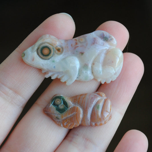 Two small stone frog carvings held in a hand against a blurred background