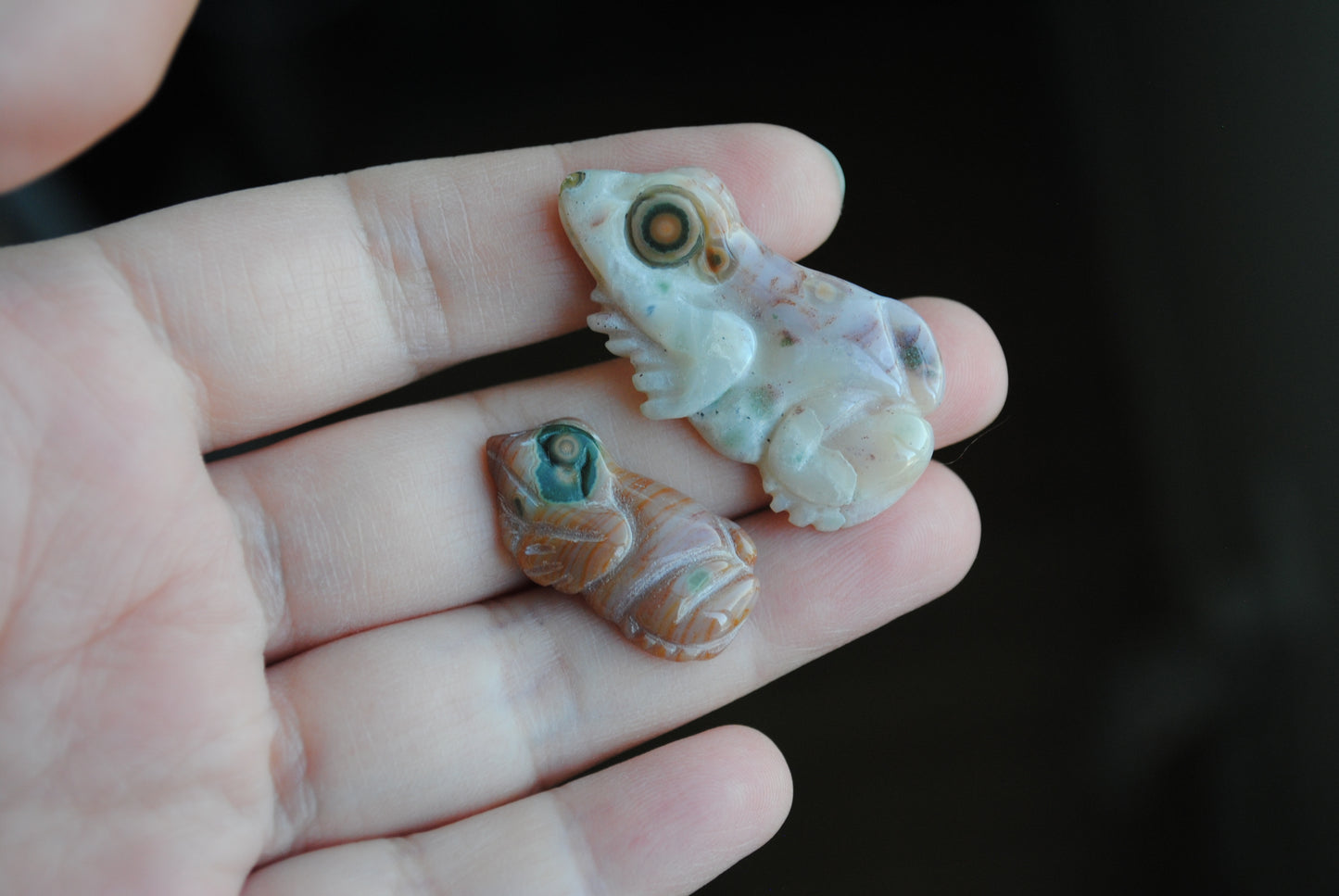 Two small stone frog carvings held in a hand against a blurred background