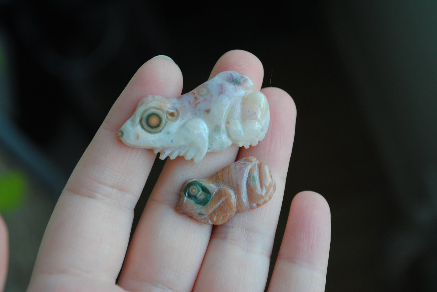 Two small stone frog carvings held in a hand against a blurred background
