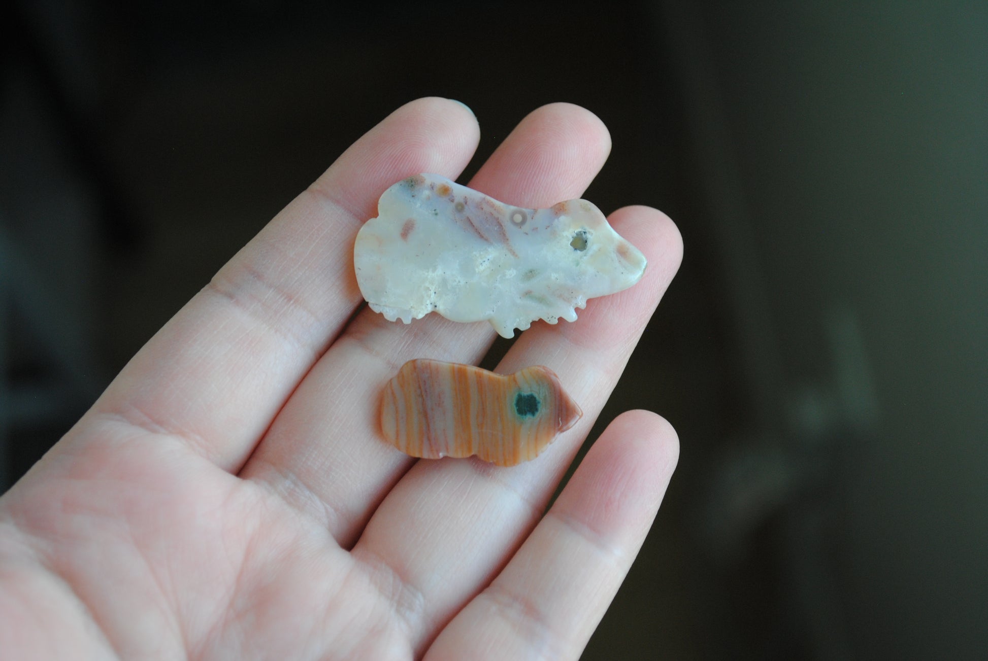 Two small stone frog carvings held in a hand against a blurred background