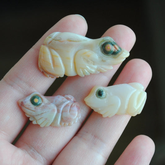 Three small stone frog carvings held in a hand against a blurred background