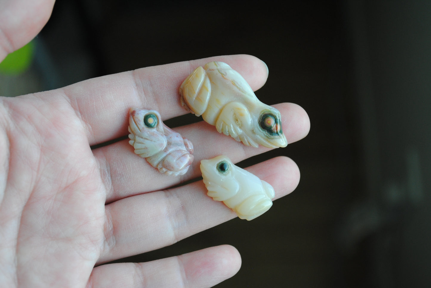 Three small stone frog carvings held in a hand against a blurred background
