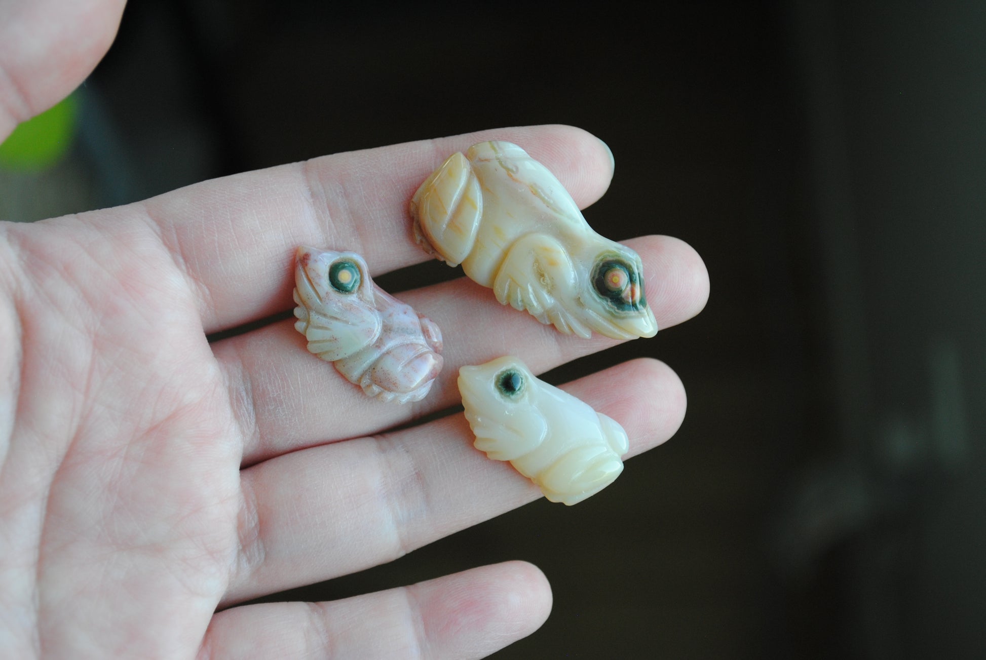 Three small stone frog carvings held in a hand against a blurred background
