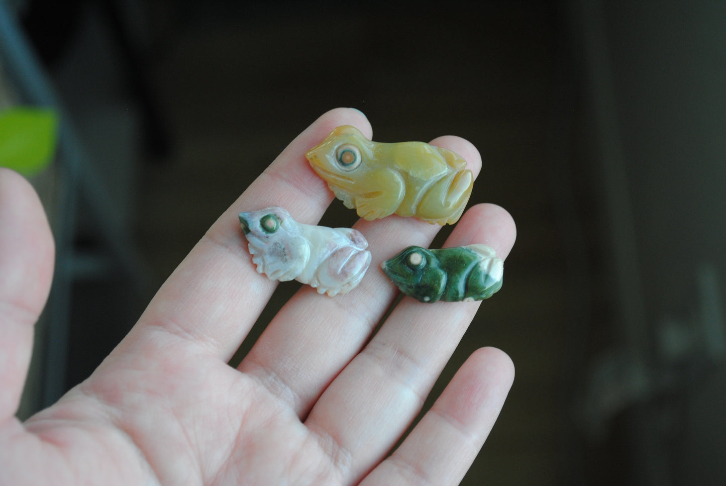 Three small stone frog carvings held in a hand against a blurred background