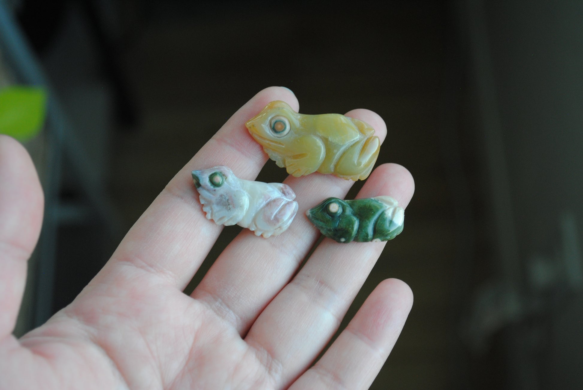 Three small stone frog carvings held in a hand against a blurred background