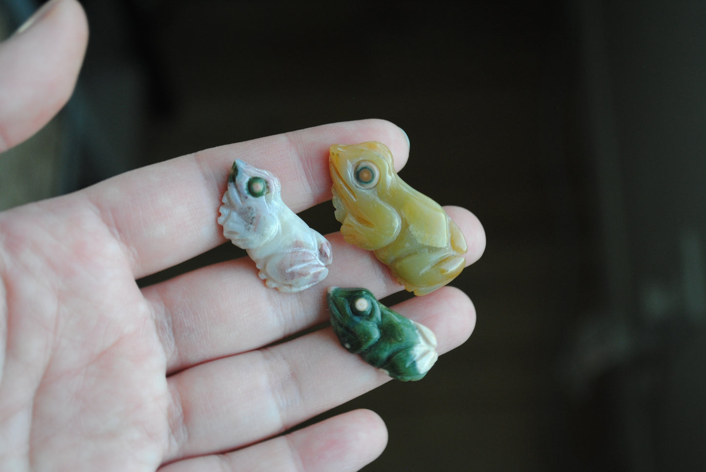 Three small stone frog carvings held in a hand against a blurred background