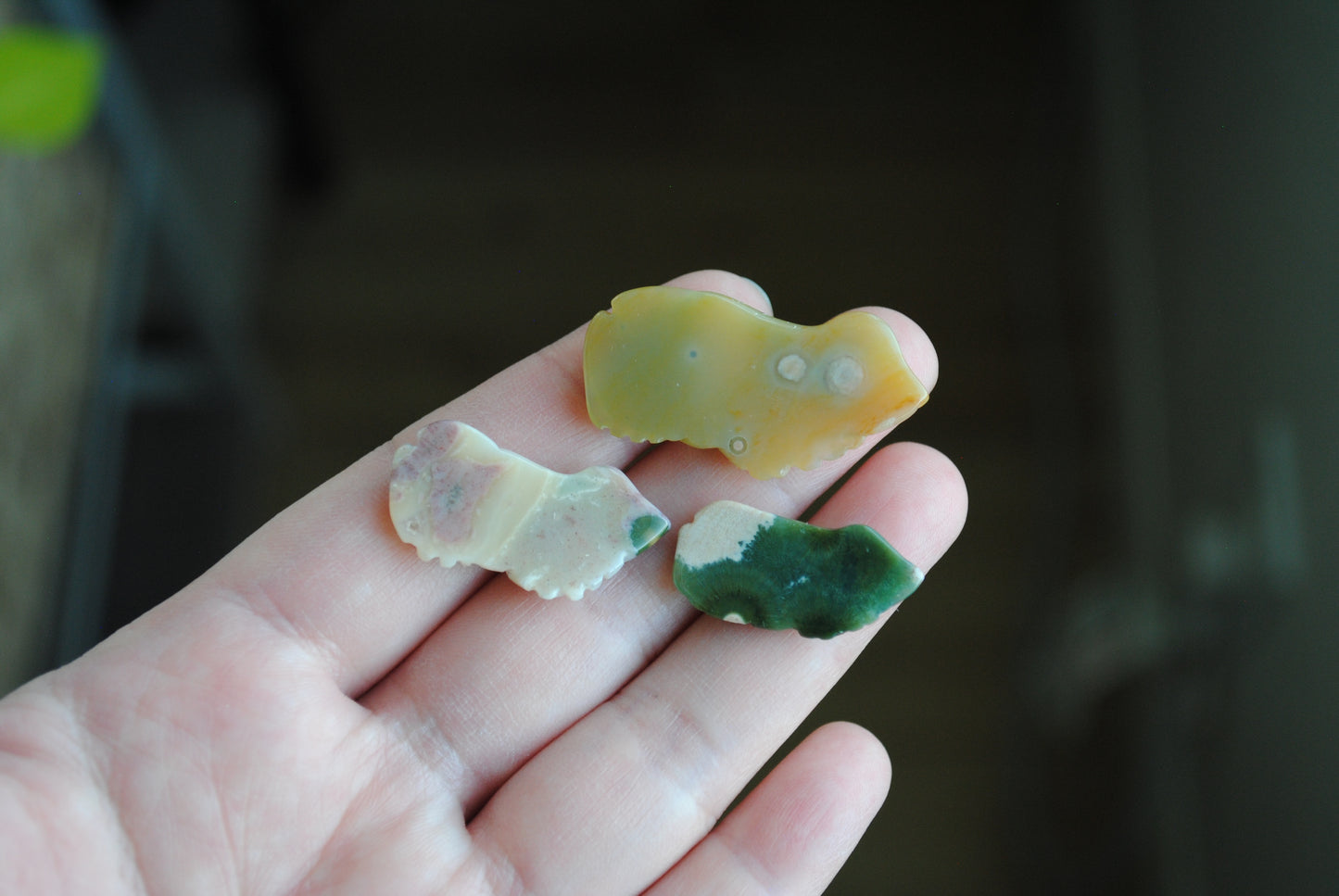 Three small stone frog carvings held in a hand against a blurred background