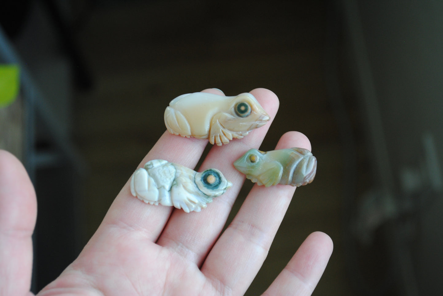 Three small stone frog carvings held in a hand against a blurred background