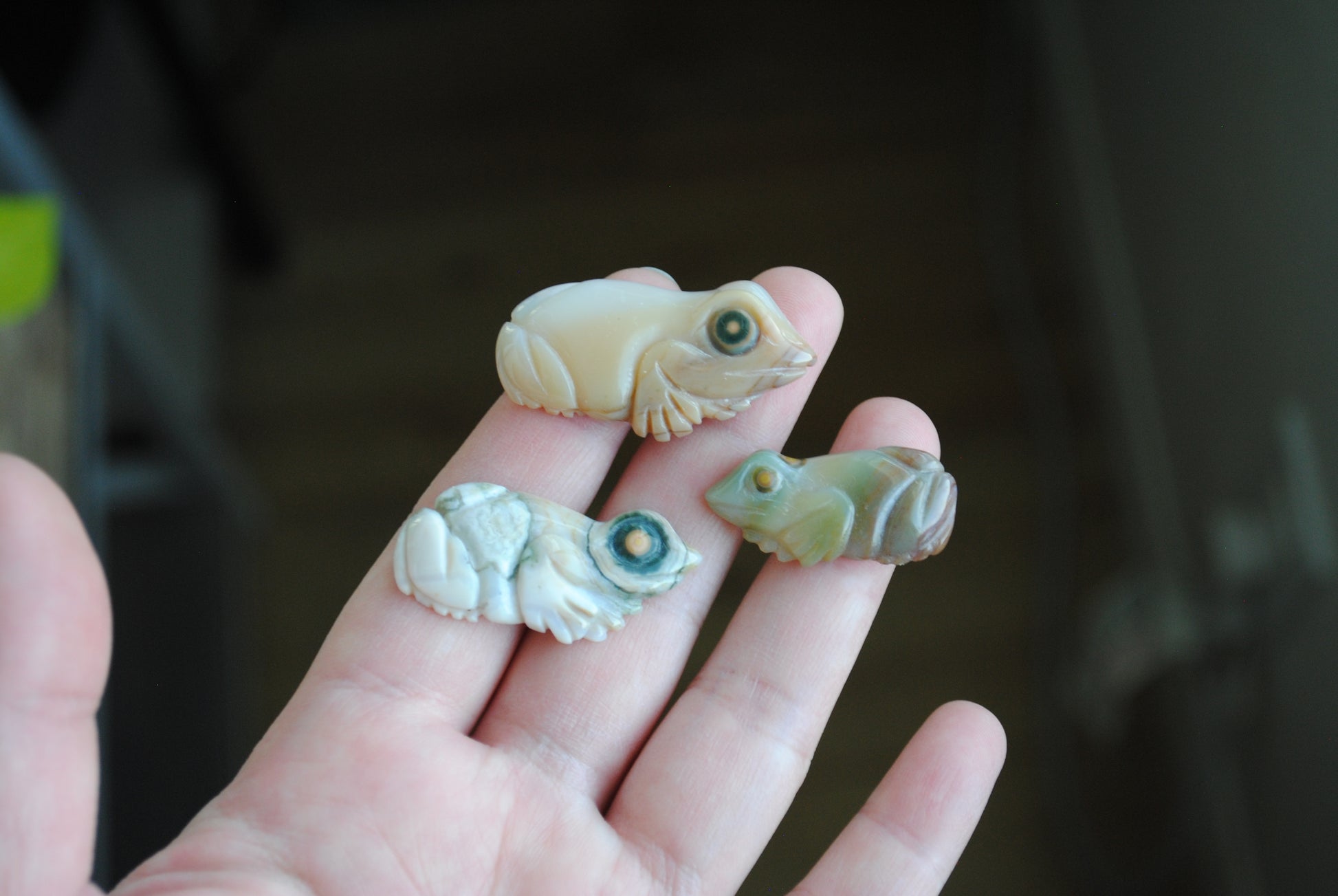 Three small stone frog carvings held in a hand against a blurred background