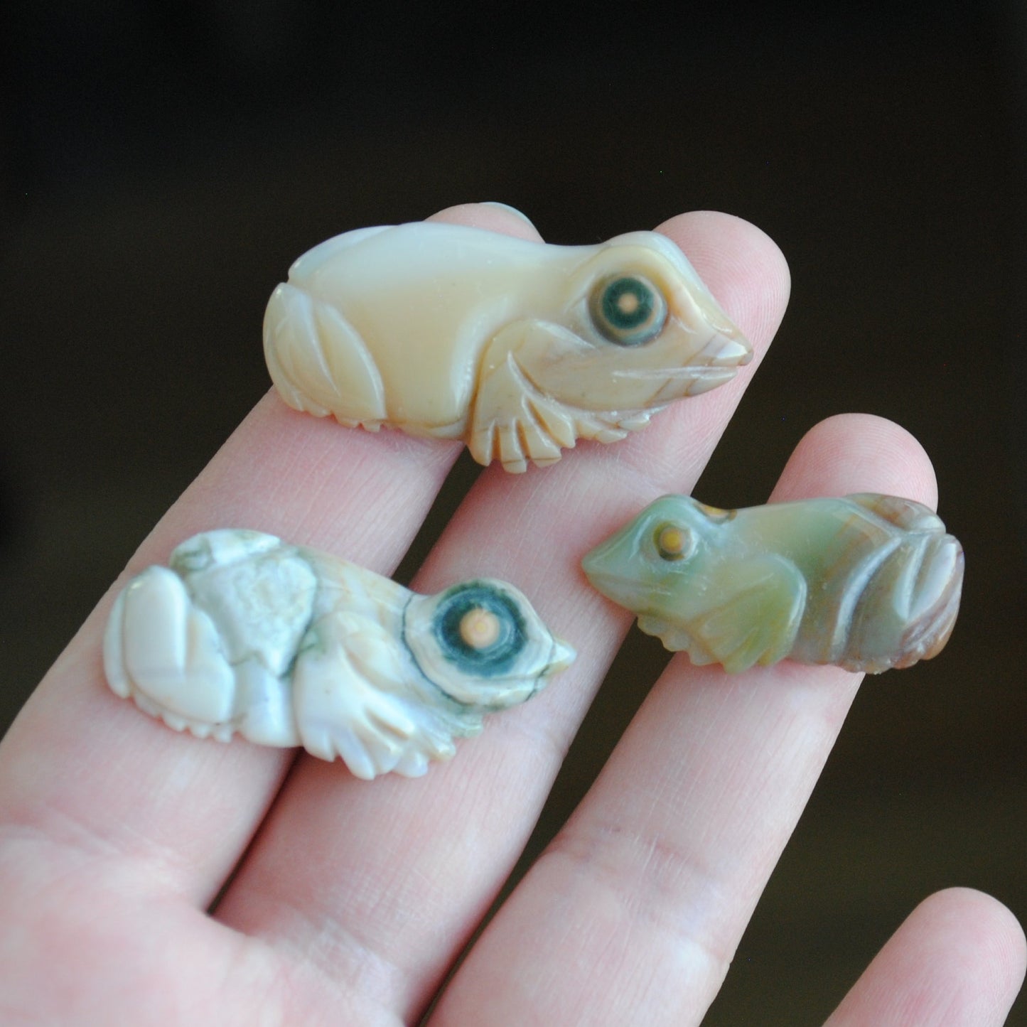 Three small stone frog carvings held in a hand against a blurred background