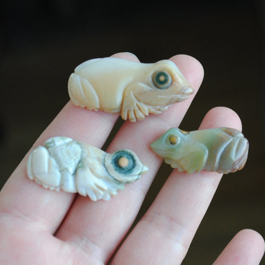 Three small stone frog carvings held in a hand against a blurred background