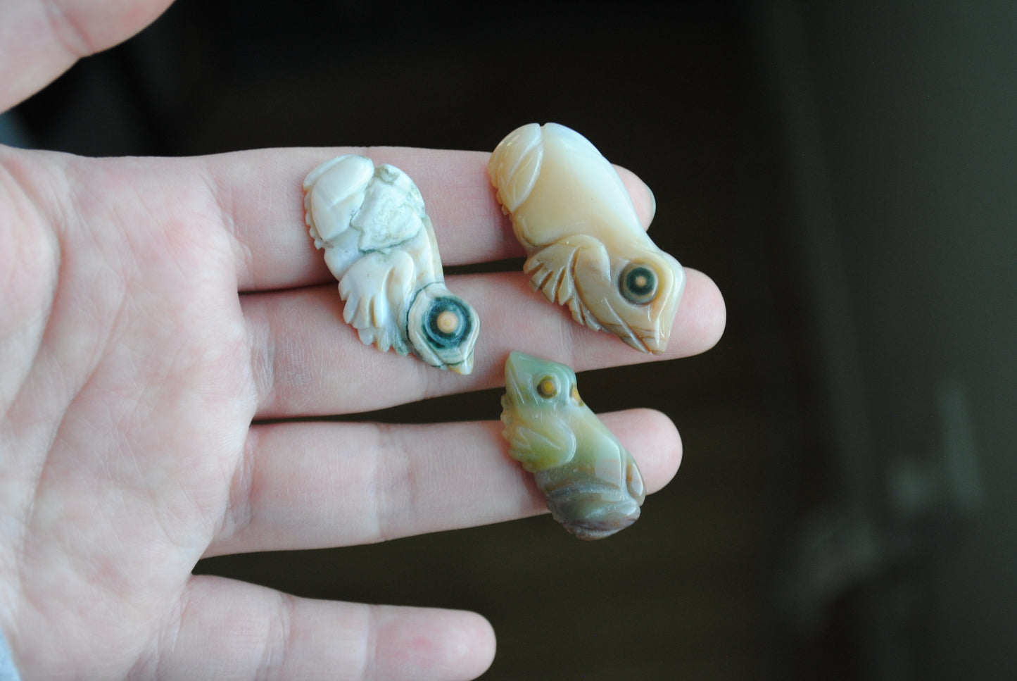 Three small stone frog carvings held in a hand against a blurred background