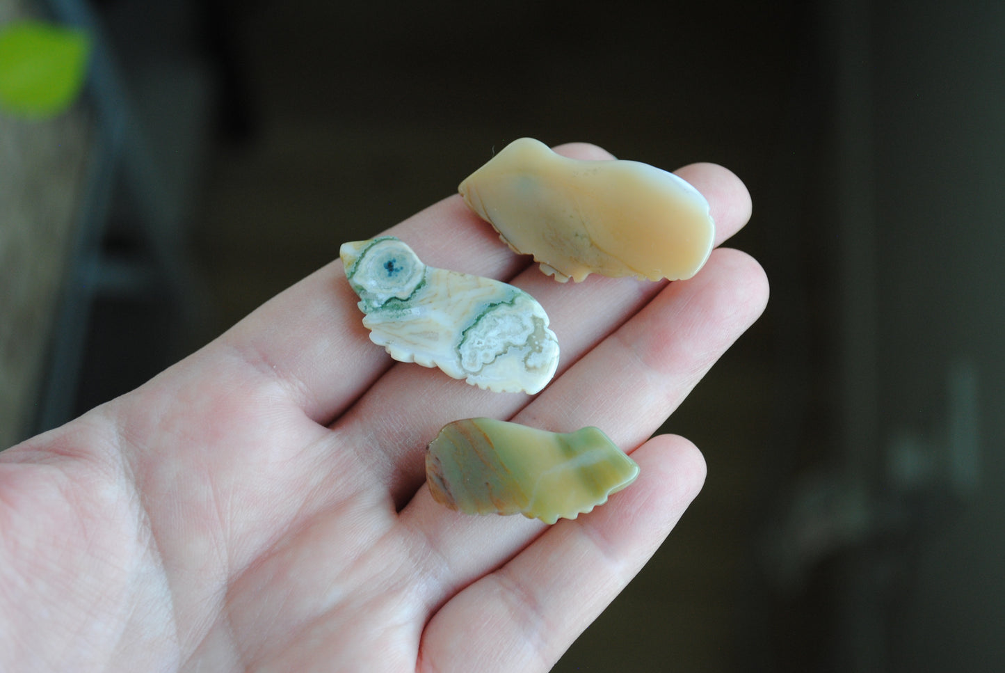 Three small stone frog carvings held in a hand against a blurred background