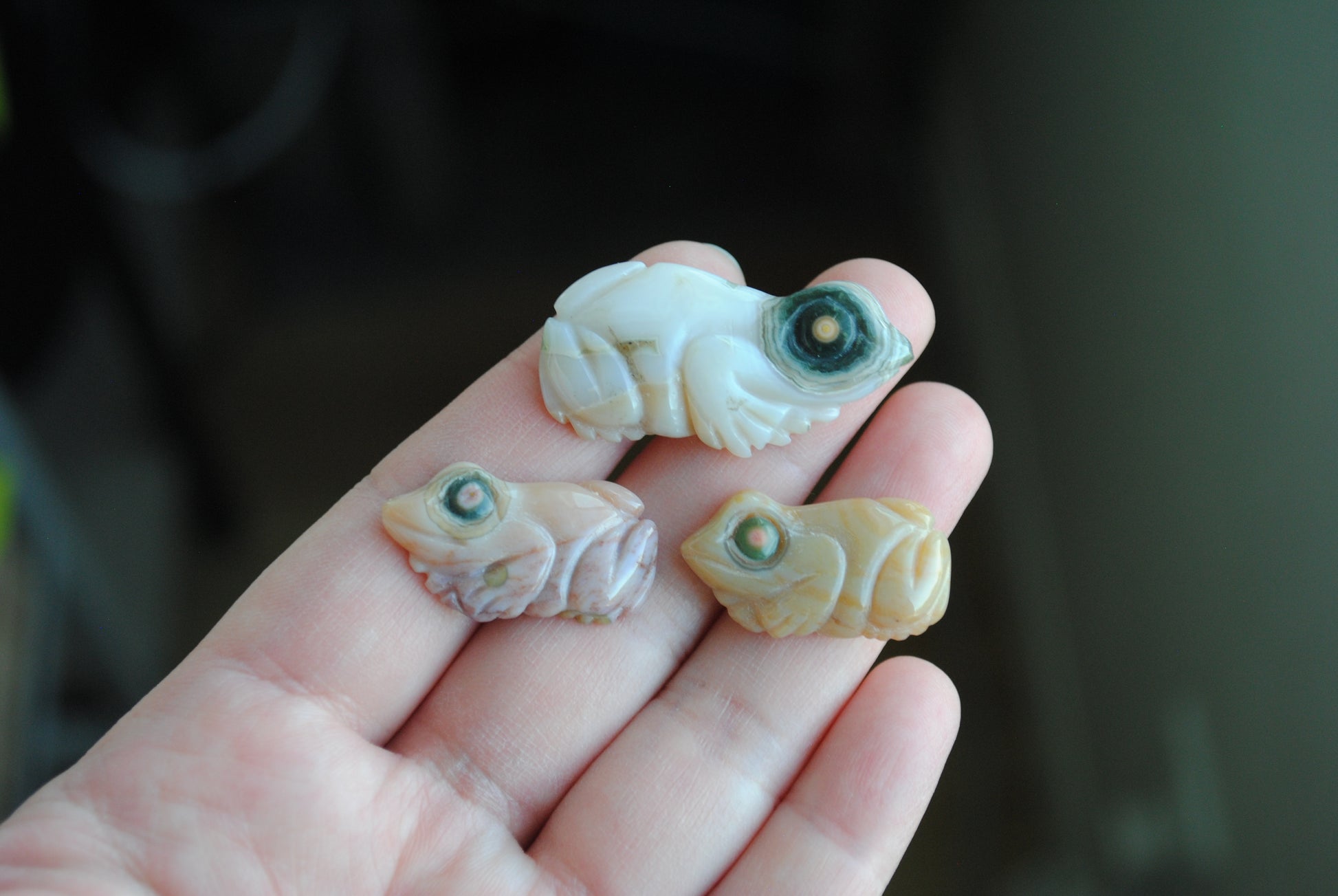 Three small stone frog carvings held in a hand against a blurred background