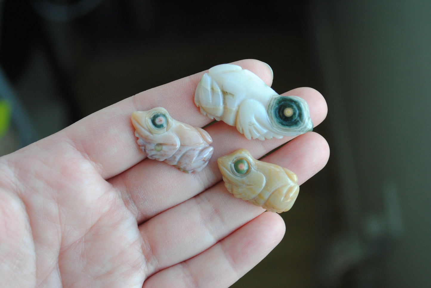 Three small stone frog carvings held in a hand against a blurred background