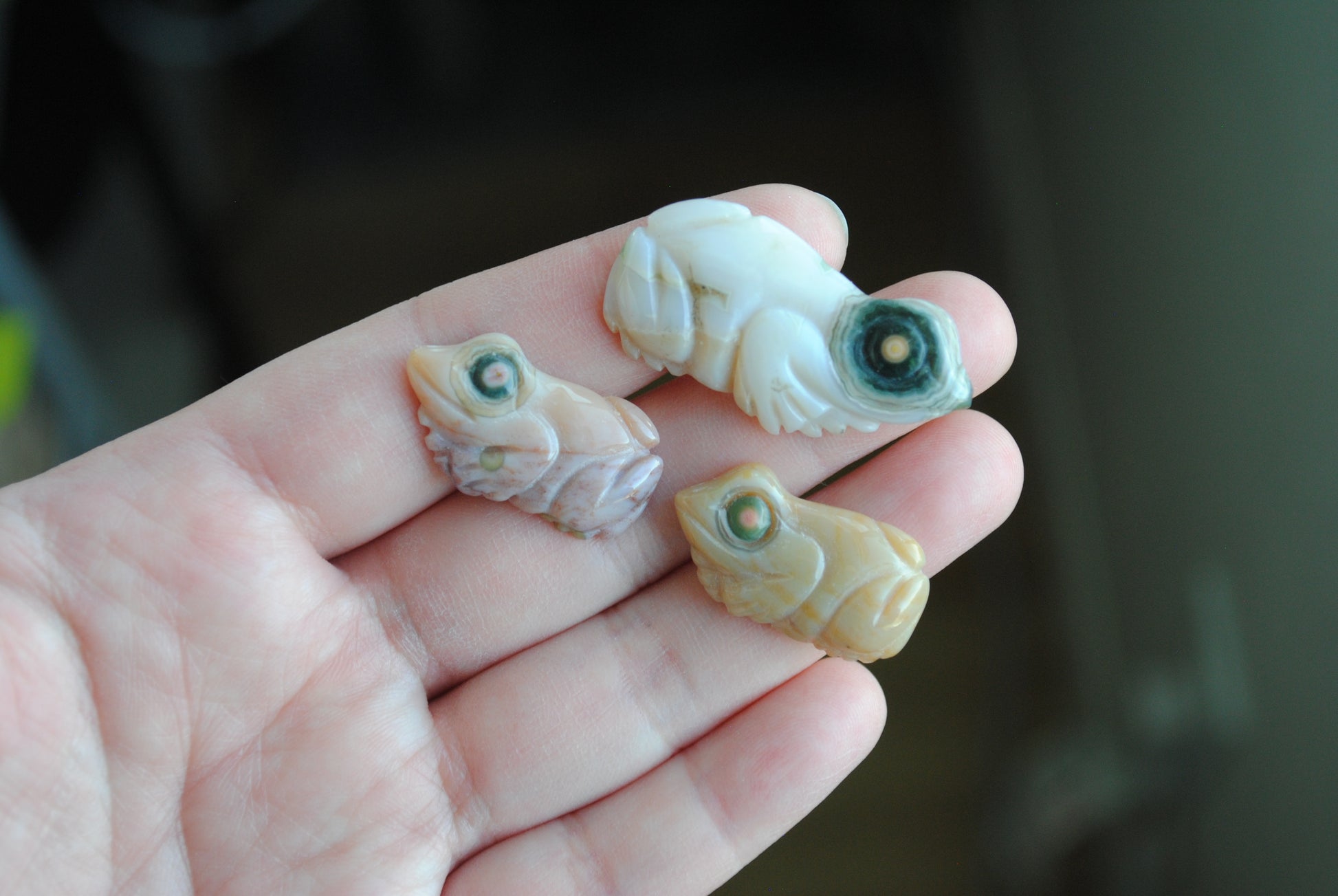 Three small stone frog carvings held in a hand against a blurred background
