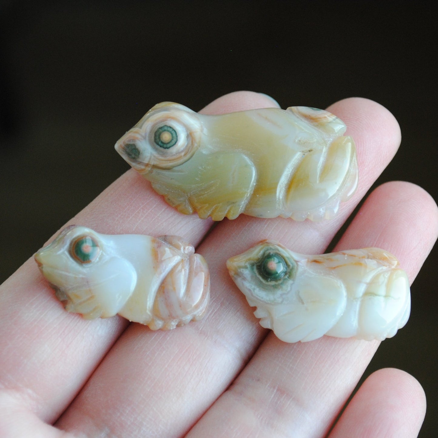 Three small stone frog carvings held in a hand against a blurred background