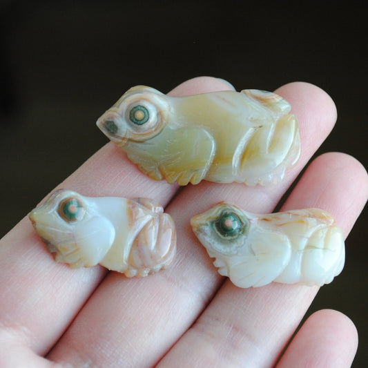 Three small stone frog carvings held in a hand against a blurred background