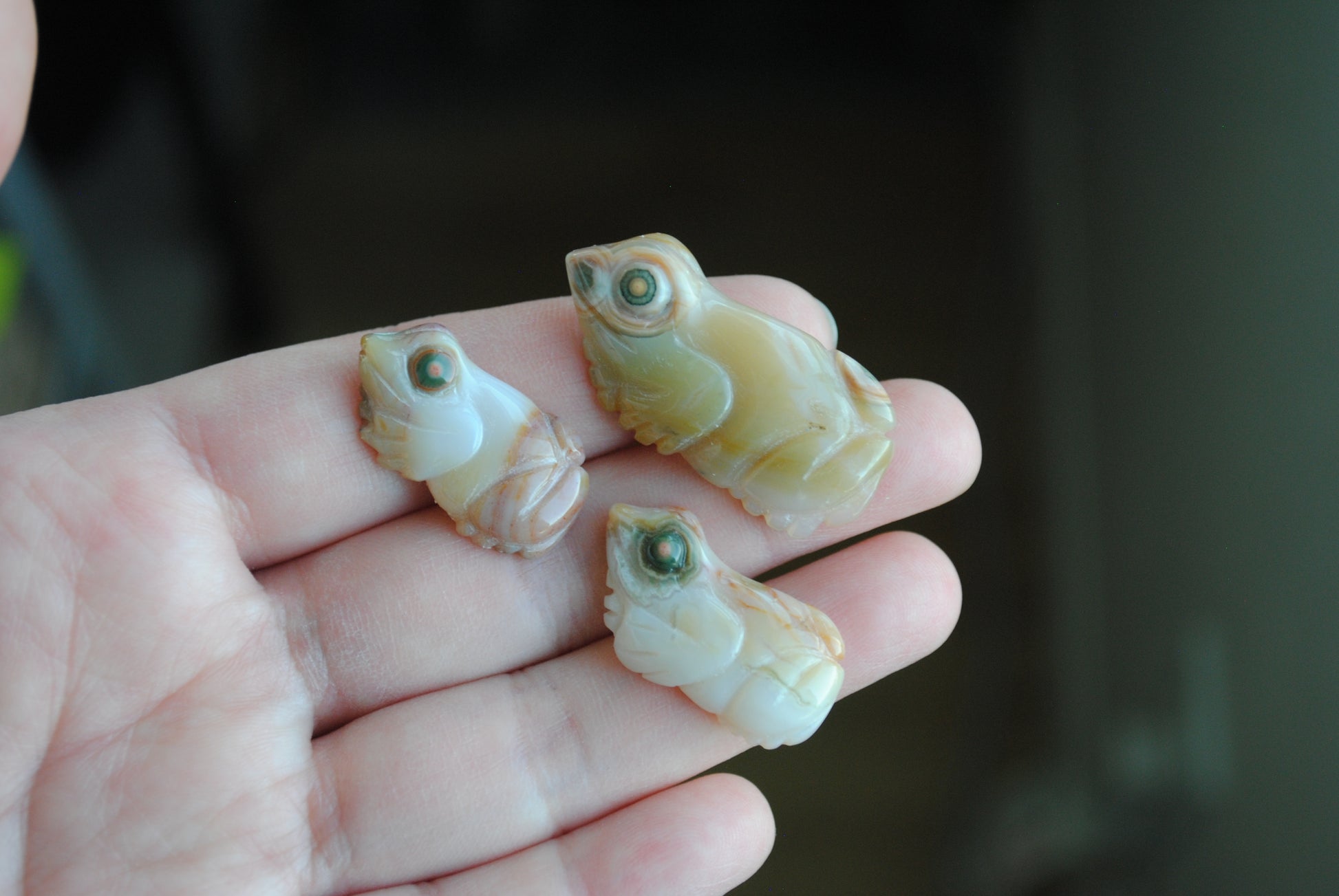 Three small stone frog carvings held in a hand against a blurred background