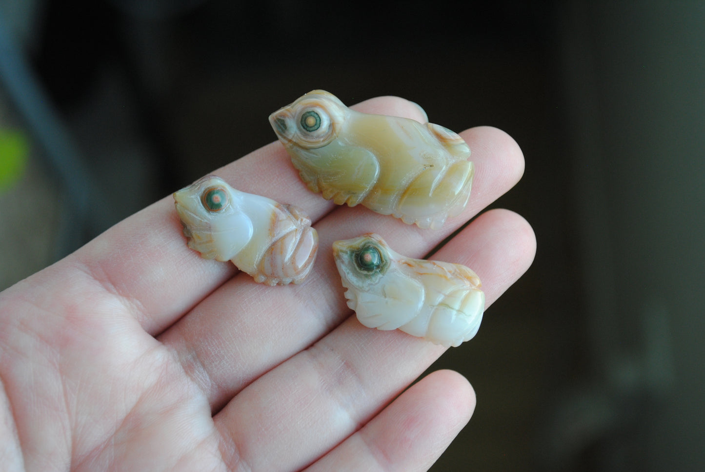 Three small stone frog carvings held in a hand against a blurred background