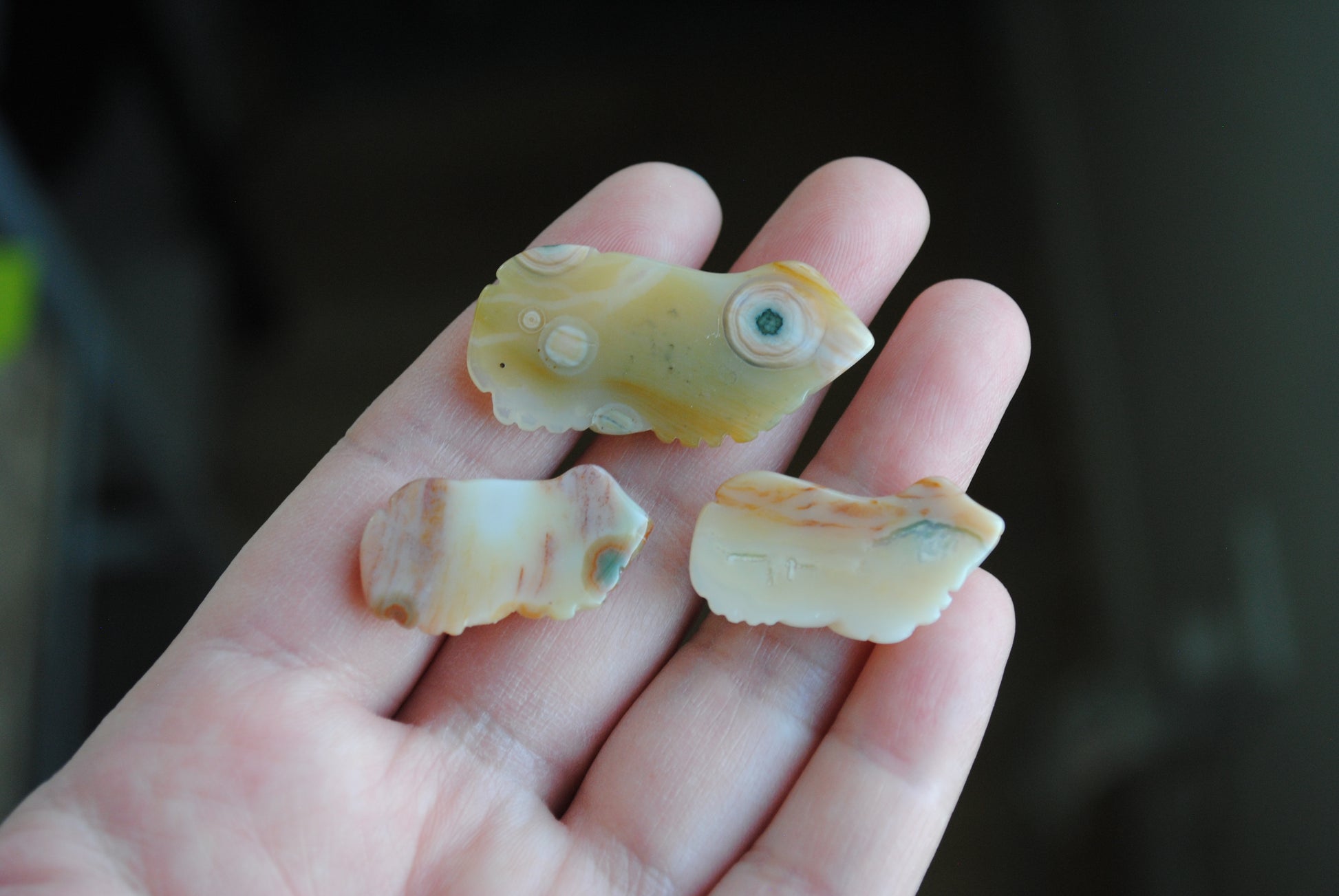 Three small stone frog carvings held in a hand against a blurred background