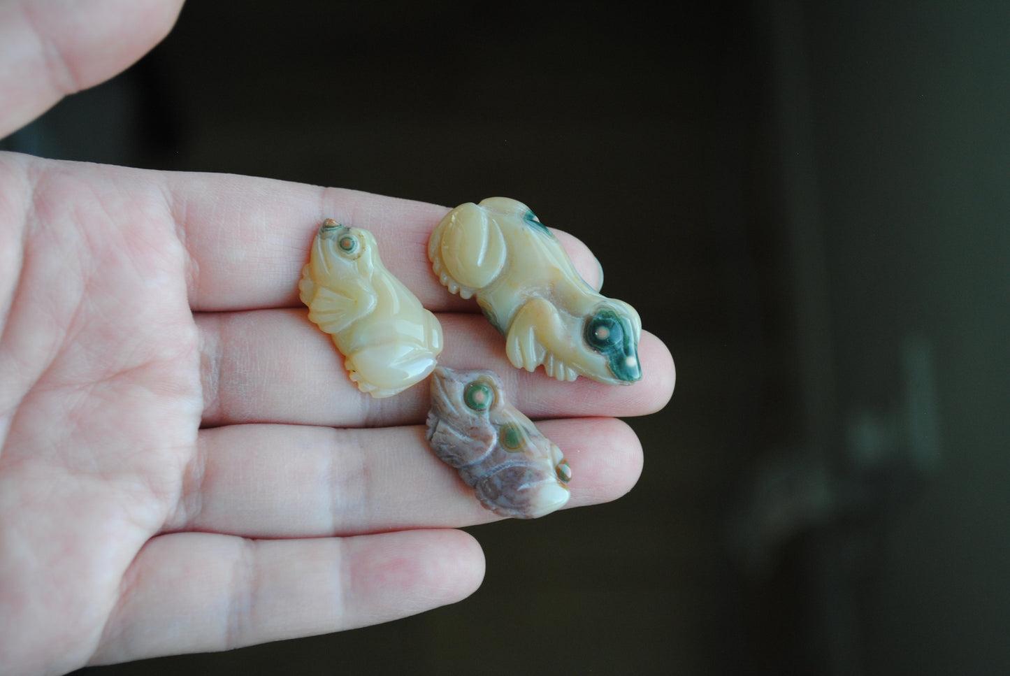 Three small stone frog carvings held in a hand against a blurred background