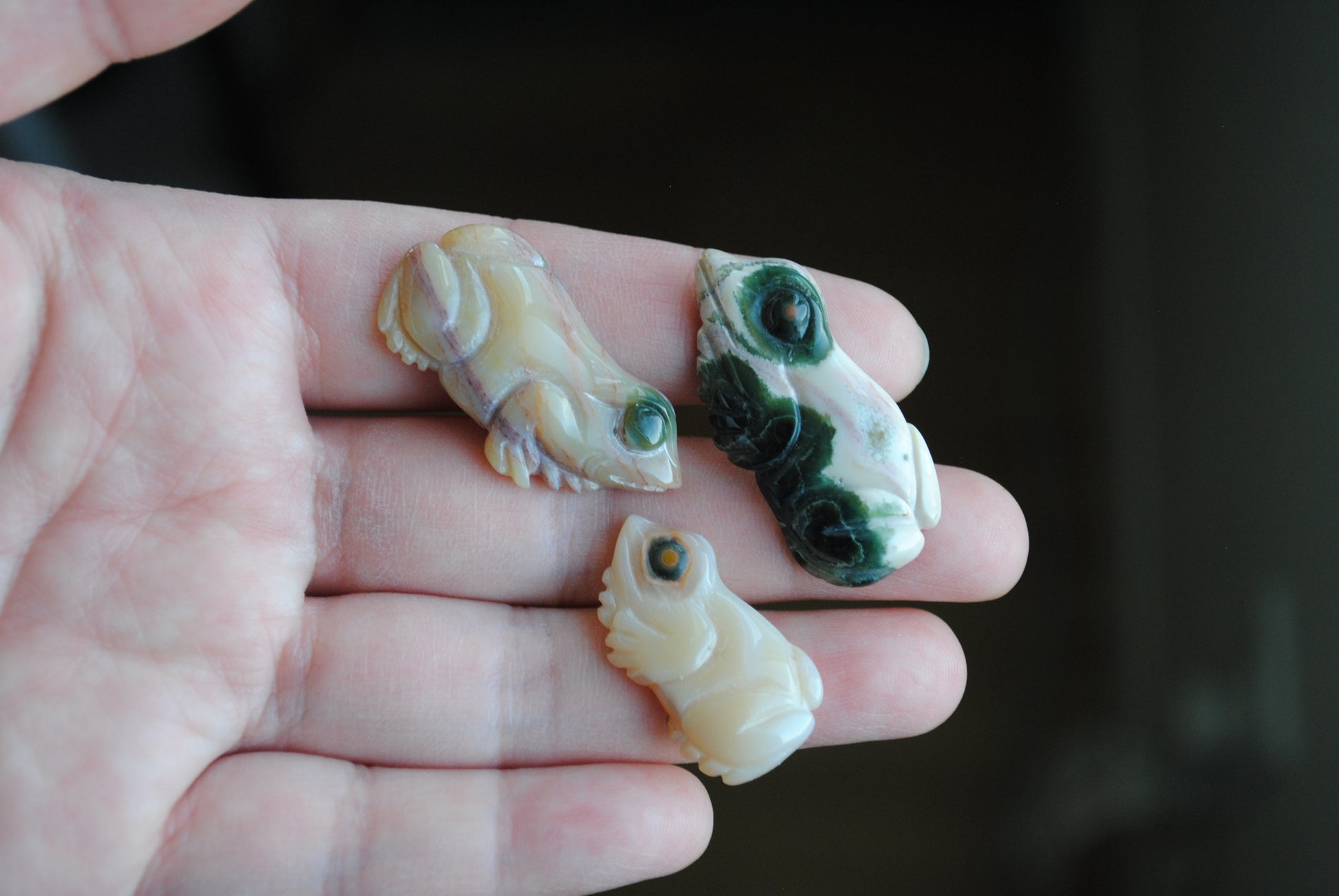 Three small stone frog carvings held in a hand against a blurred background