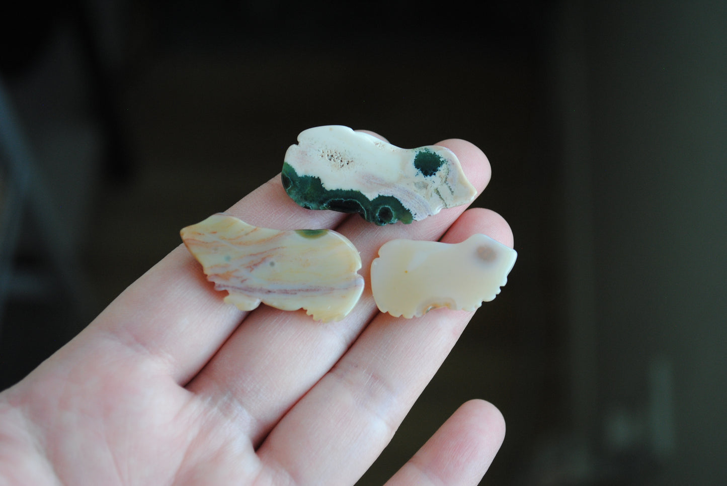 Three small stone frog carvings held in a hand against a blurred background