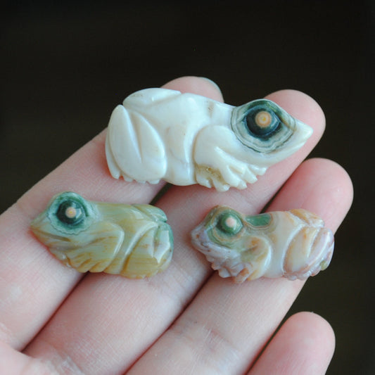 Three small stone frog carvings held in a hand against a blurred background