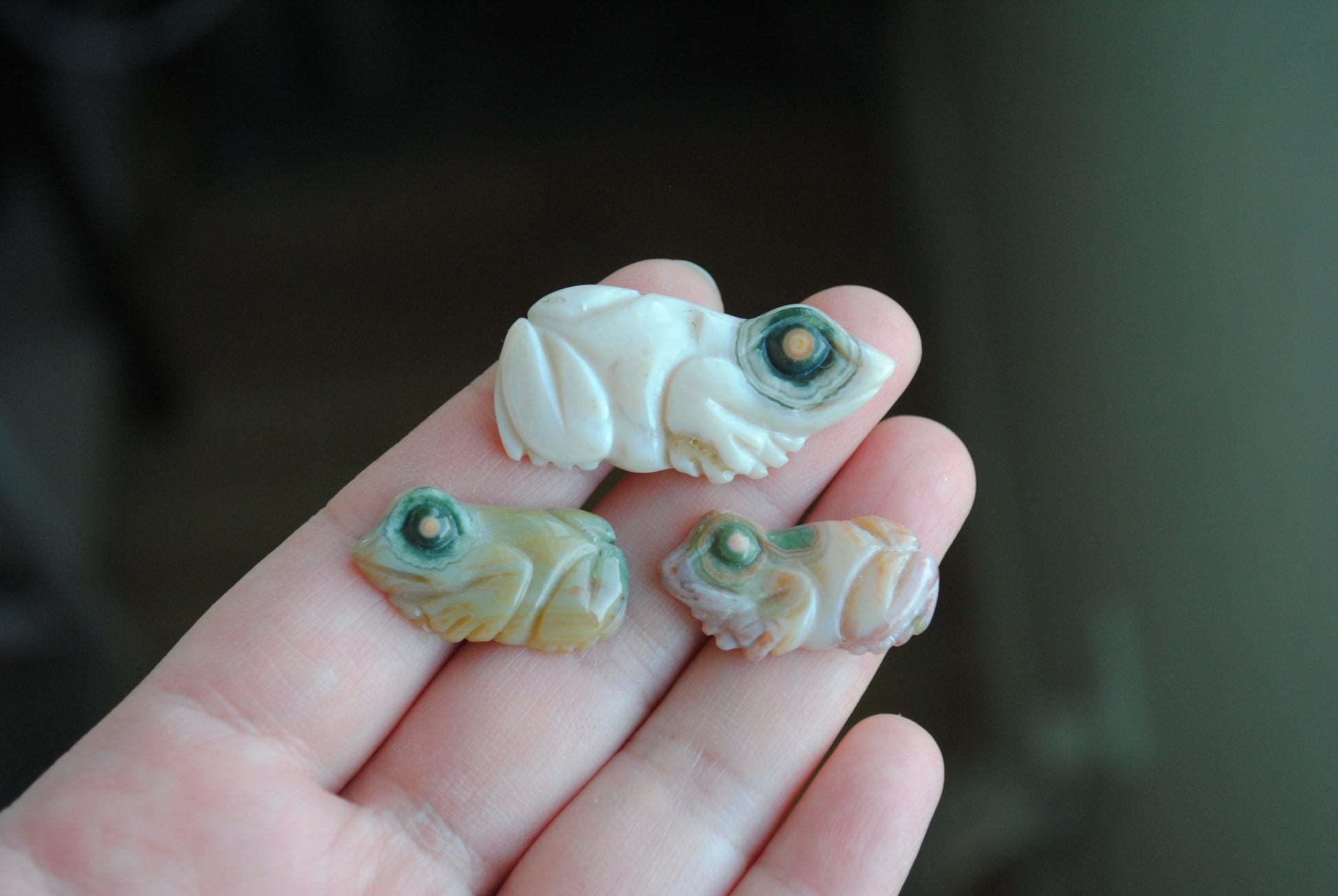 Three small stone frog carvings held in a hand against a blurred background