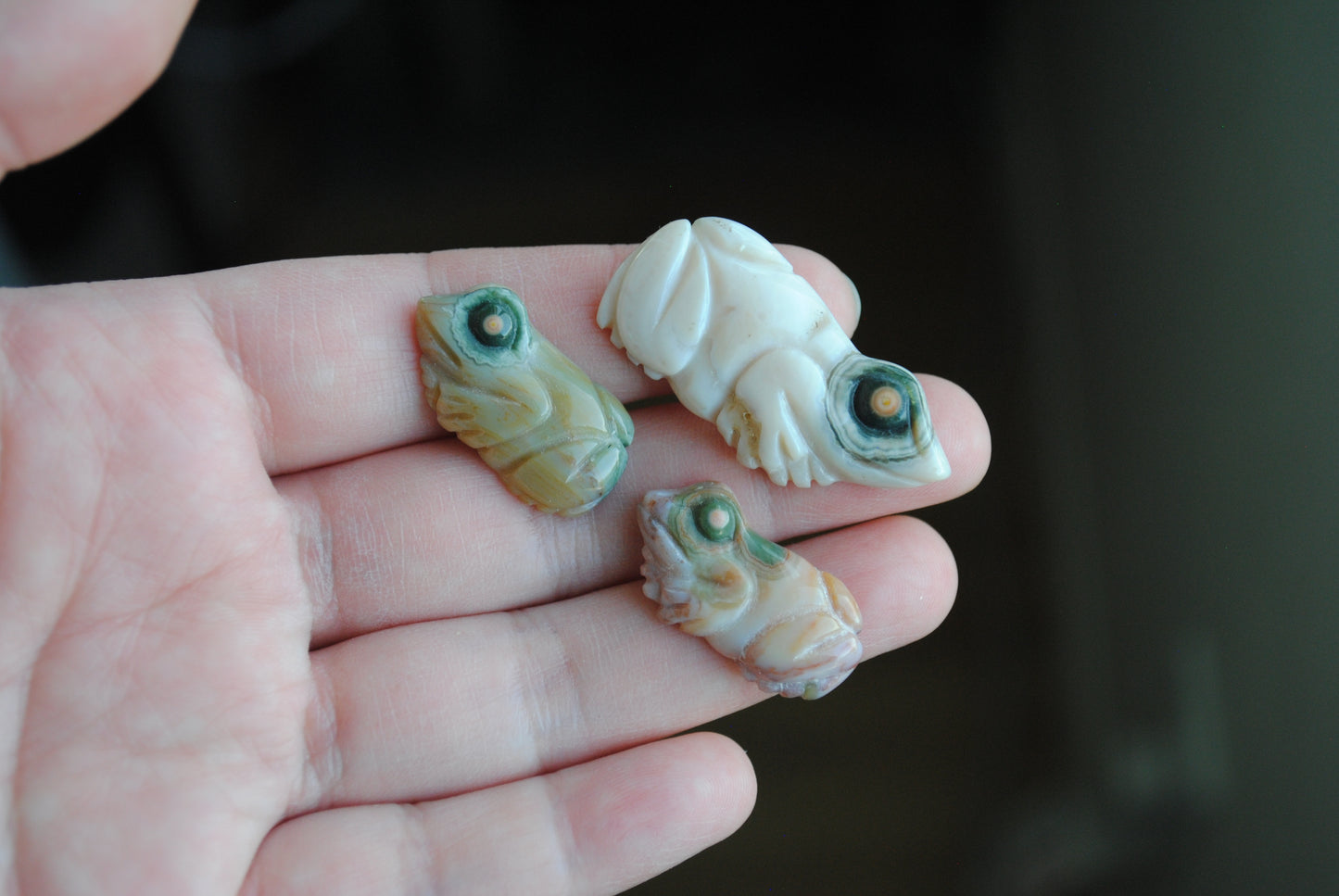 Three small stone frog carvings held in a hand against a blurred background