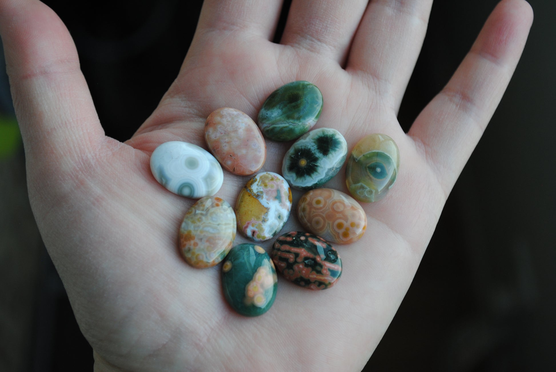Hand holding a collection of colorful stones with a dark background