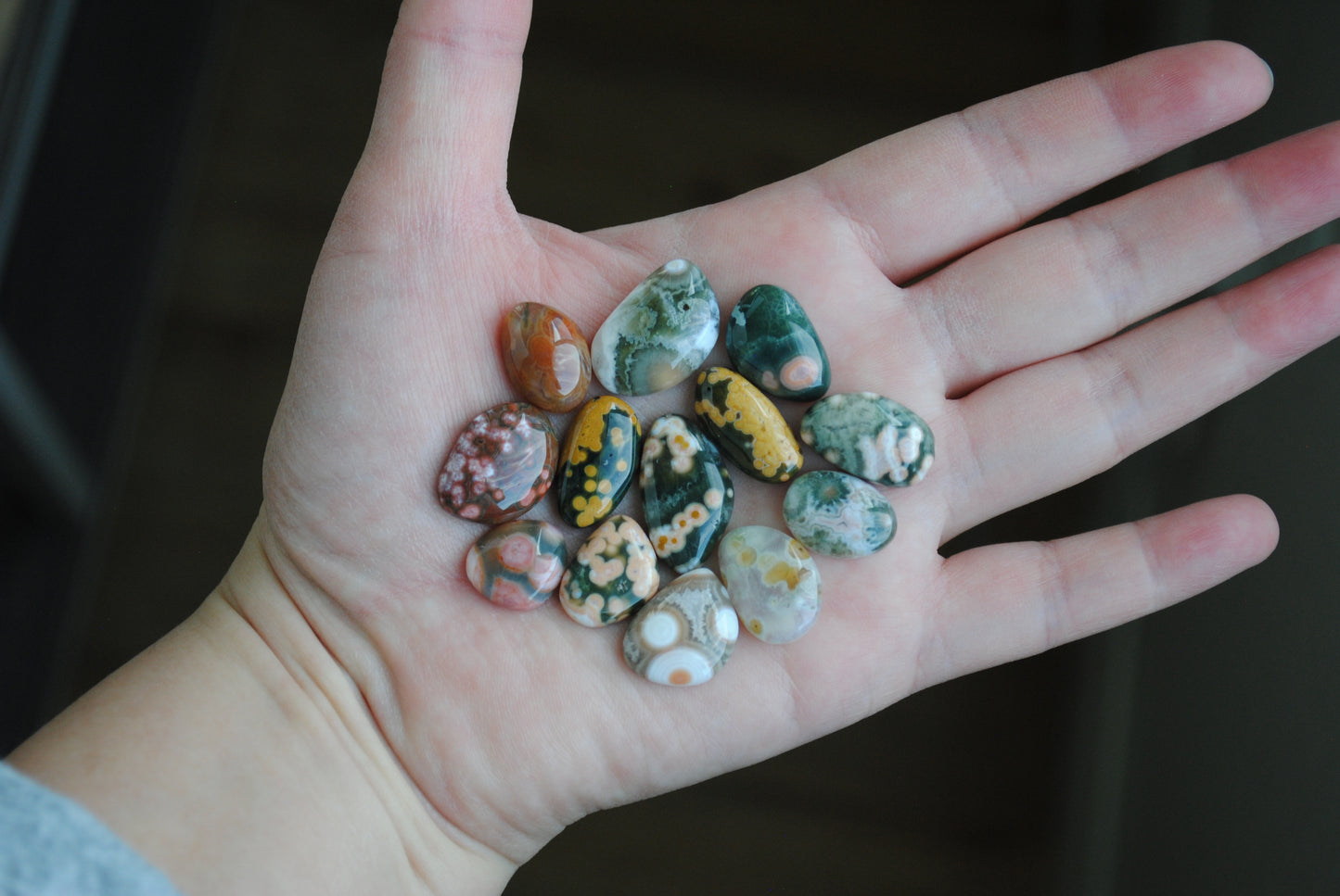 Hand holding a collection of small, multicolored stones against a dark background