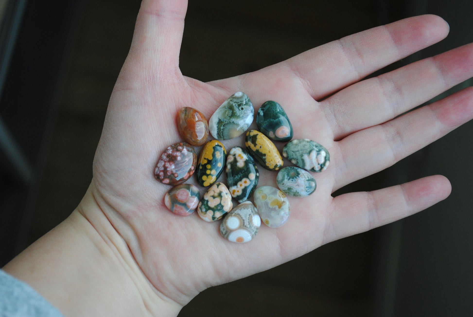 Hand holding a collection of small, multicolored stones against a dark background