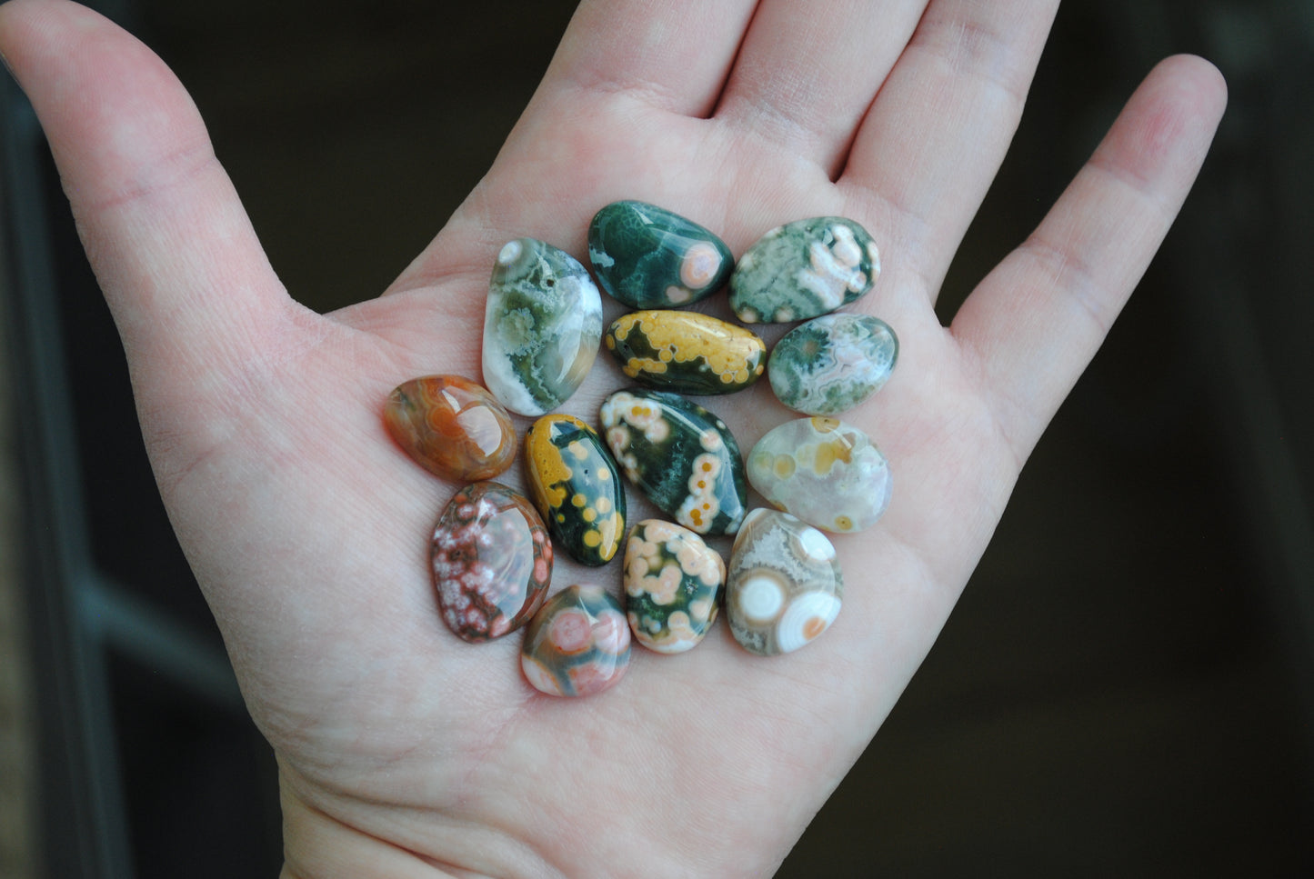 Hand holding a collection of multicolored stones against a dark background