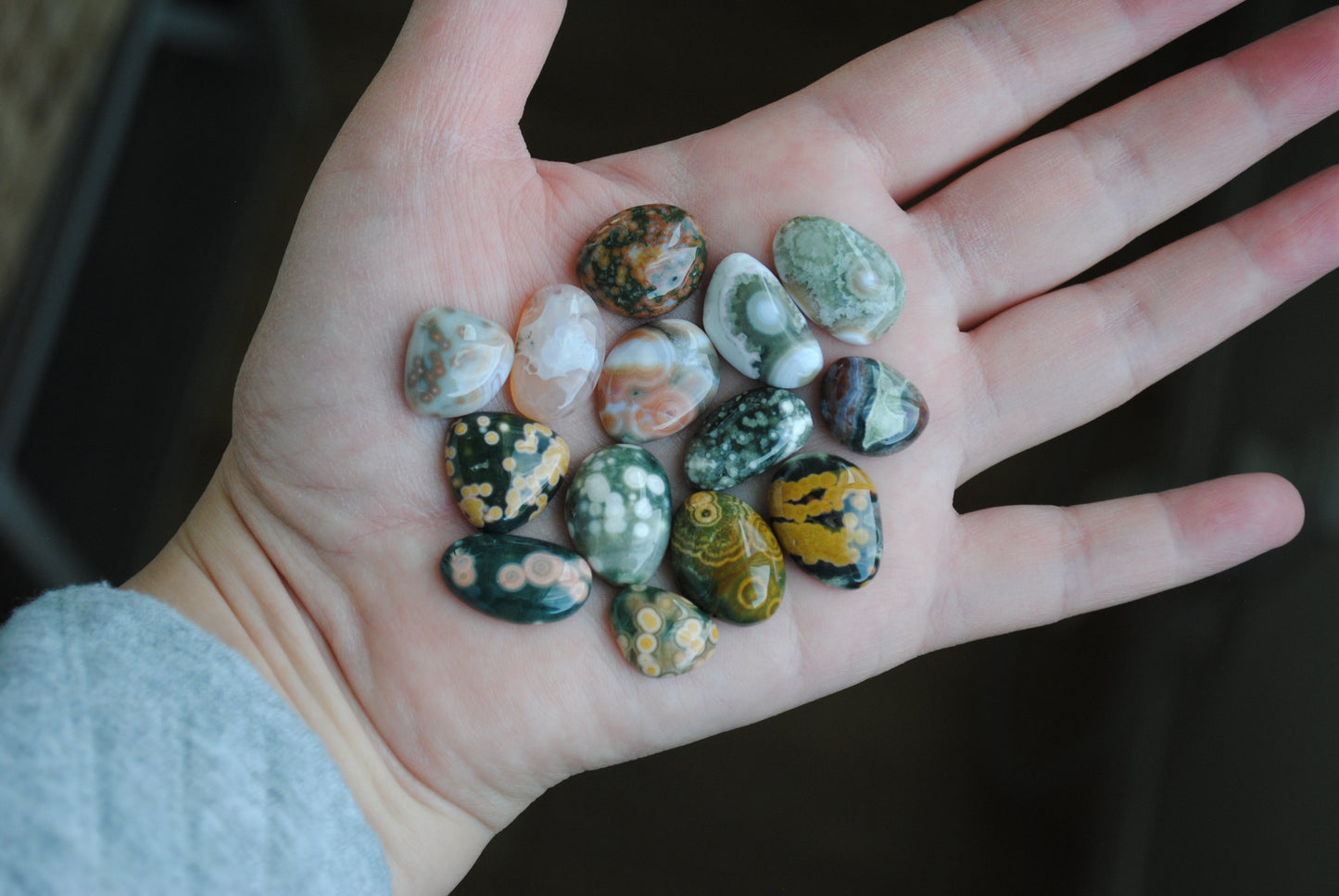 Hand holding a collection of small, multicolored stones against a dark background