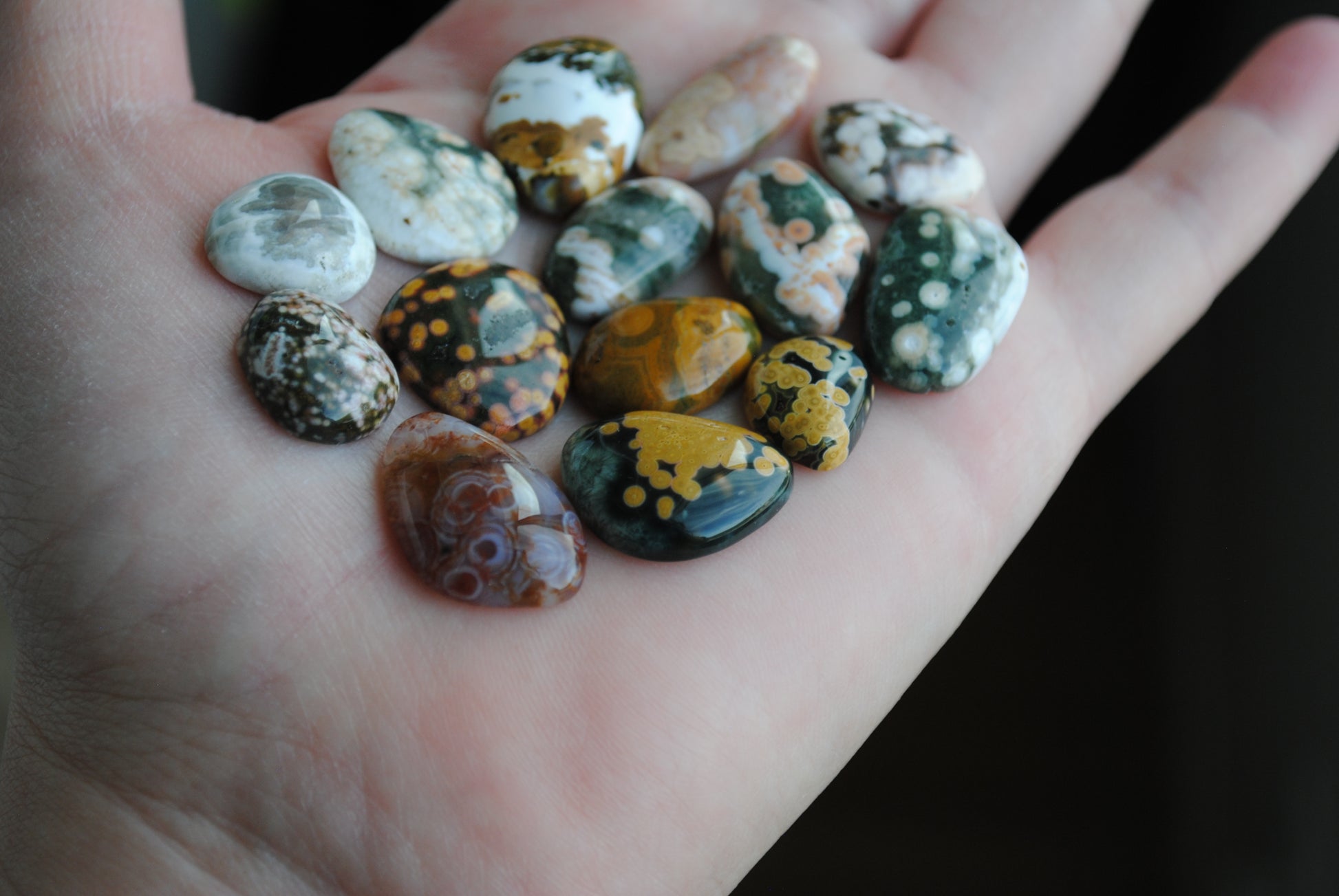 Hand holding a collection of multicolored marbled stones against a dark background