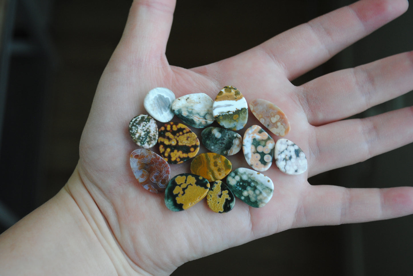 Hand holding a collection of small, multicolored stones against a dark background