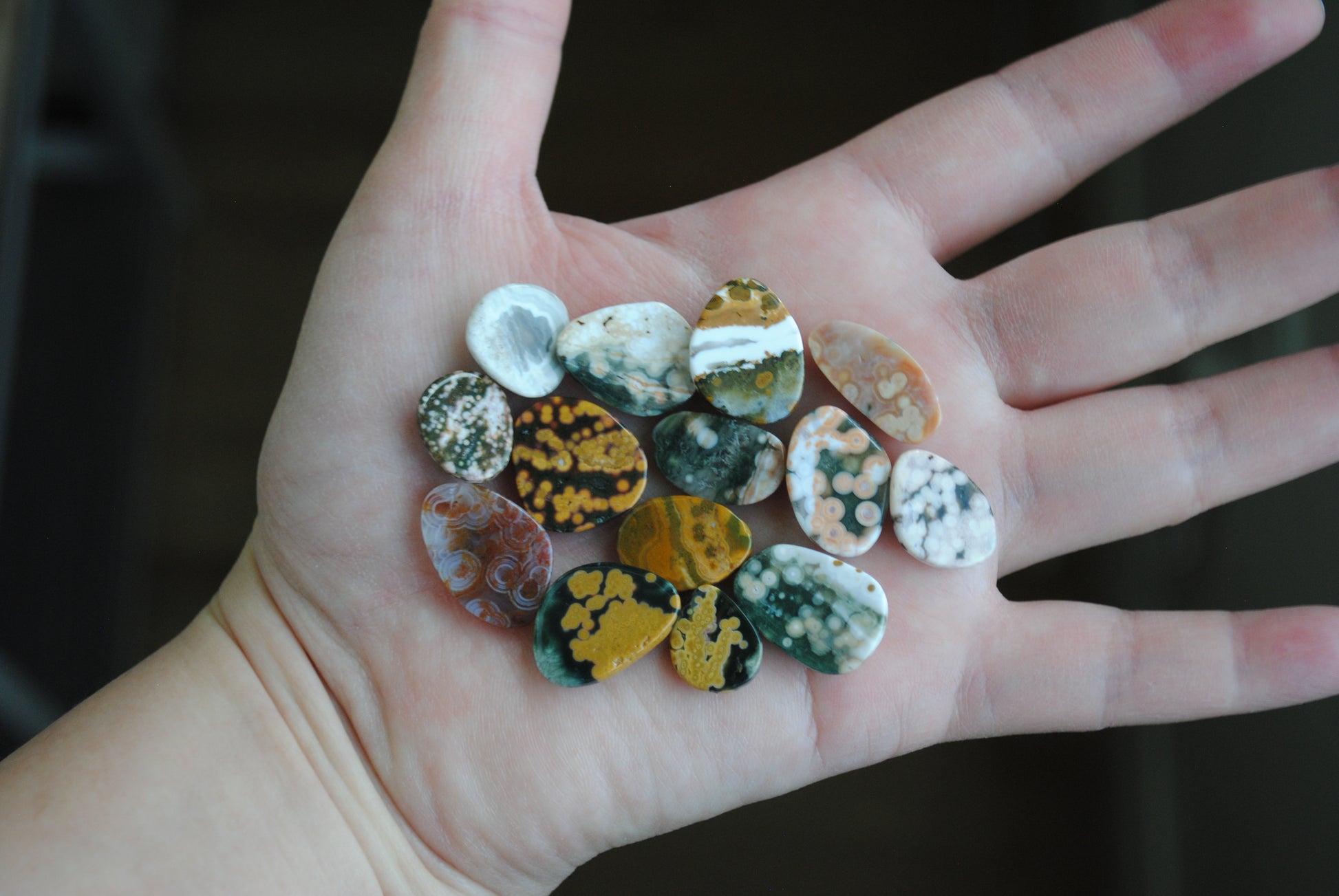 Hand holding a collection of small, multicolored stones against a dark background