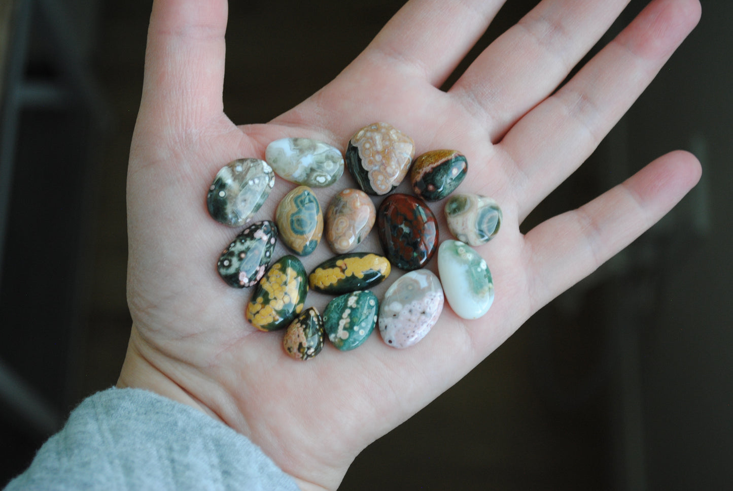 Hand holding a small collection of multicolored stones against a dark background