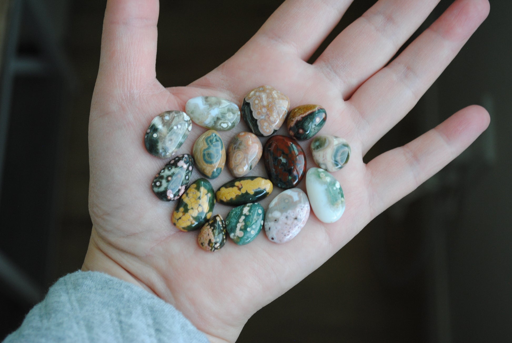 Hand holding a small collection of multicolored stones against a dark background