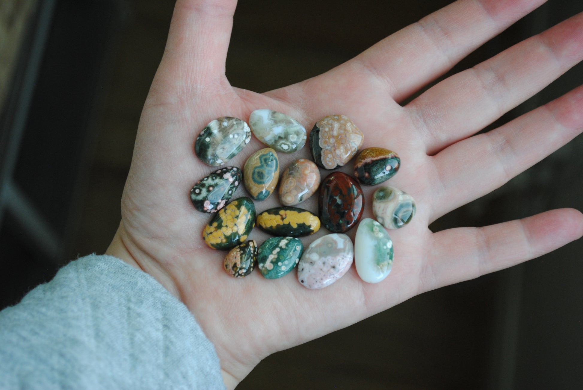 Hand holding a collection of small, multicolored stones against a dark background