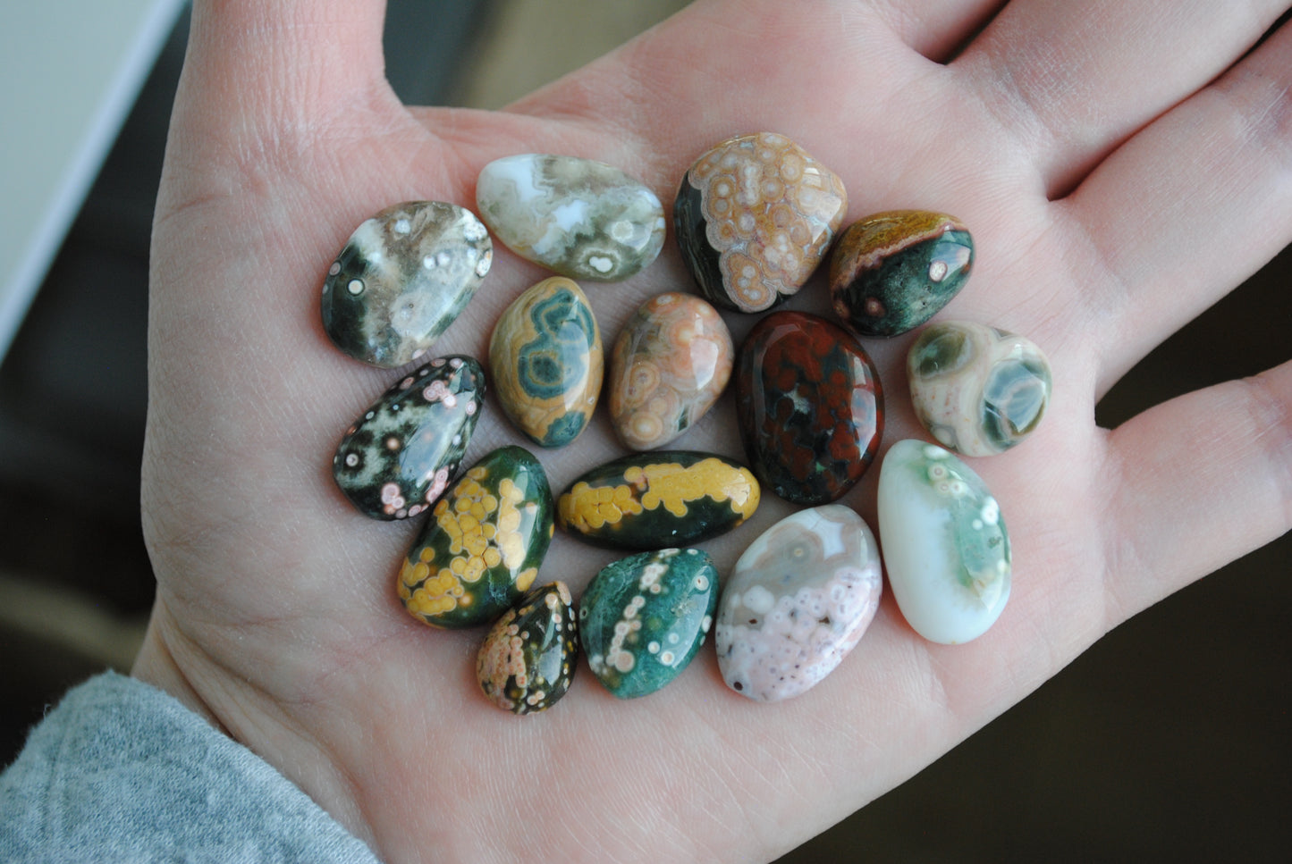 Hand holding a collection of multicolored stones with a blurred background