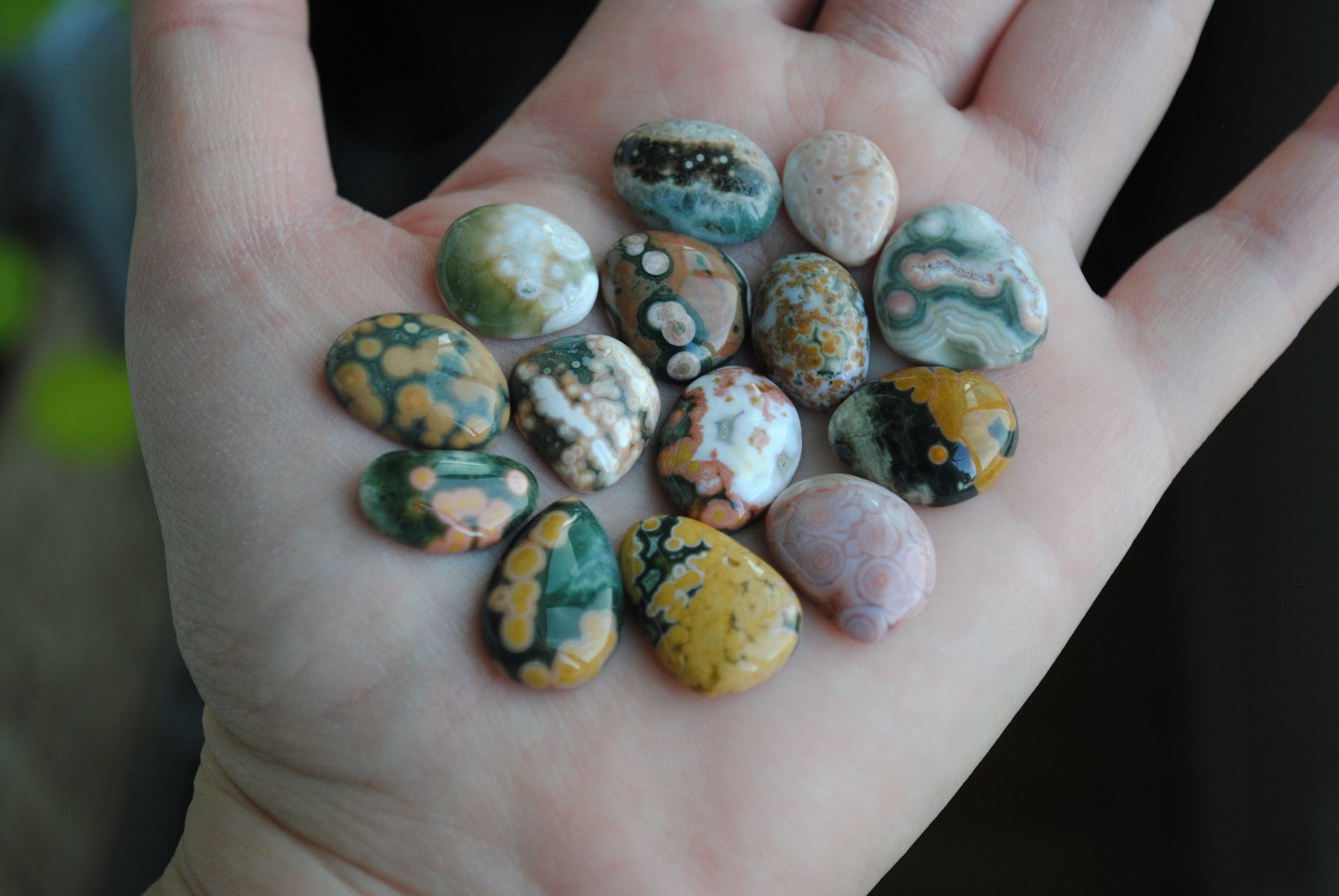 Hand holding a collection of multicolored stones with a blurred natural background